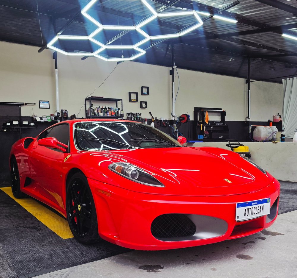 Ferrari vermelha com a placa AUTOCLEAN dentro da oficina, sob iluminação em formato hexagonal.